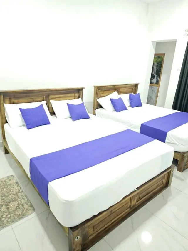 Two beds with violet runners and blue pillows by the window