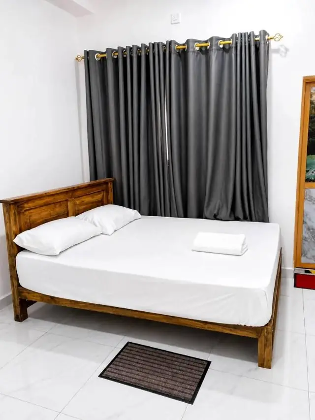 Double bed with crisp white linen, carved wooden headboard and blackout curtains