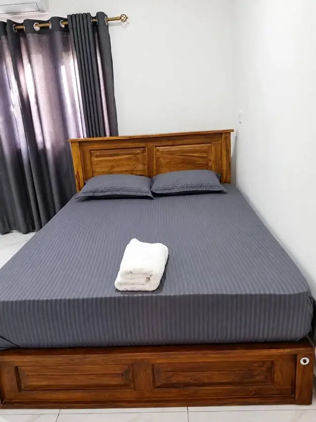 Double bed with grey linen, rolled towels and a carved wooden headboard
