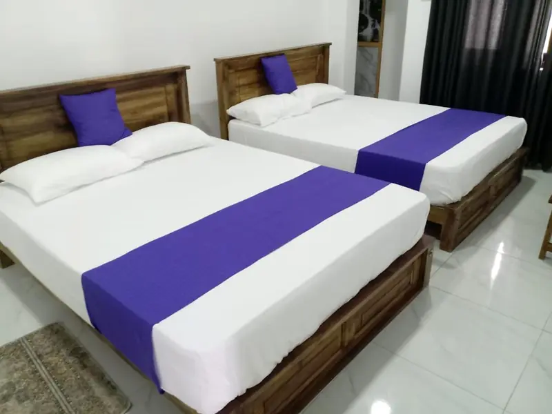 Bright room with two beds dressed in white linen and violet runners on a polished tiled floor